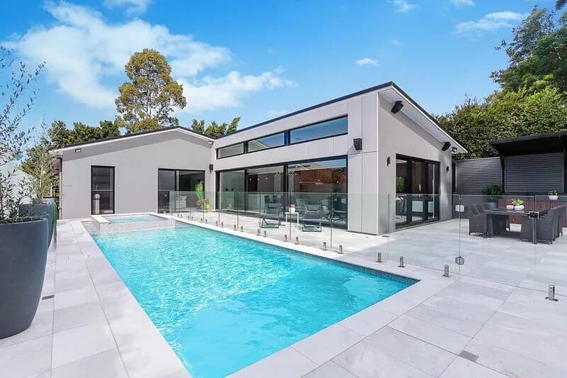 Hunters Hill Residence pool area with pale paving, glass fencing, and connected outdoor living spaces